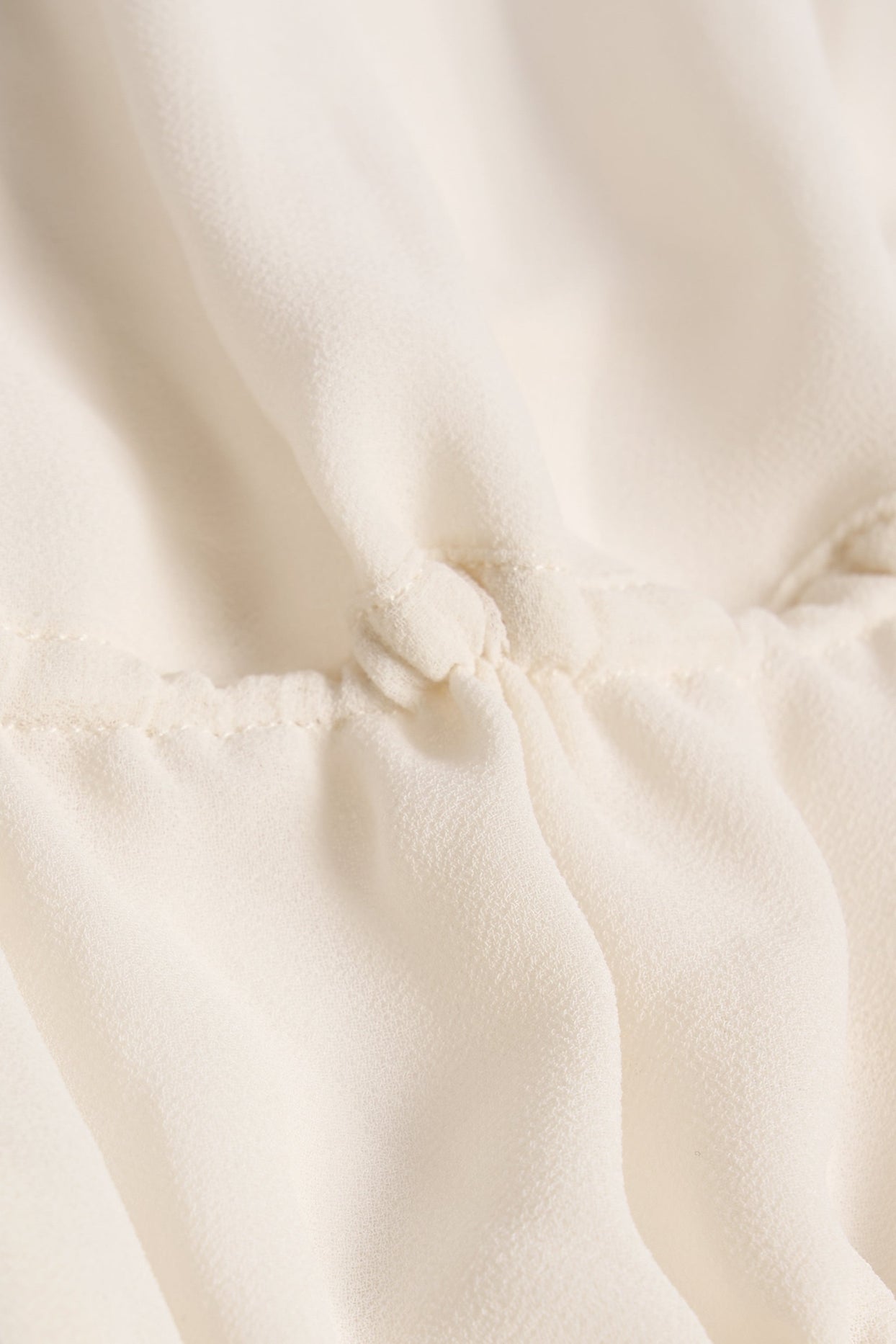 بلوزة قصيرة شبه شفافة مكشكشة، بفتحة رقبة دائرية، بلون عاجي